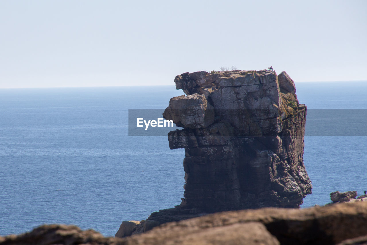 Rock formation in sea against clear sky