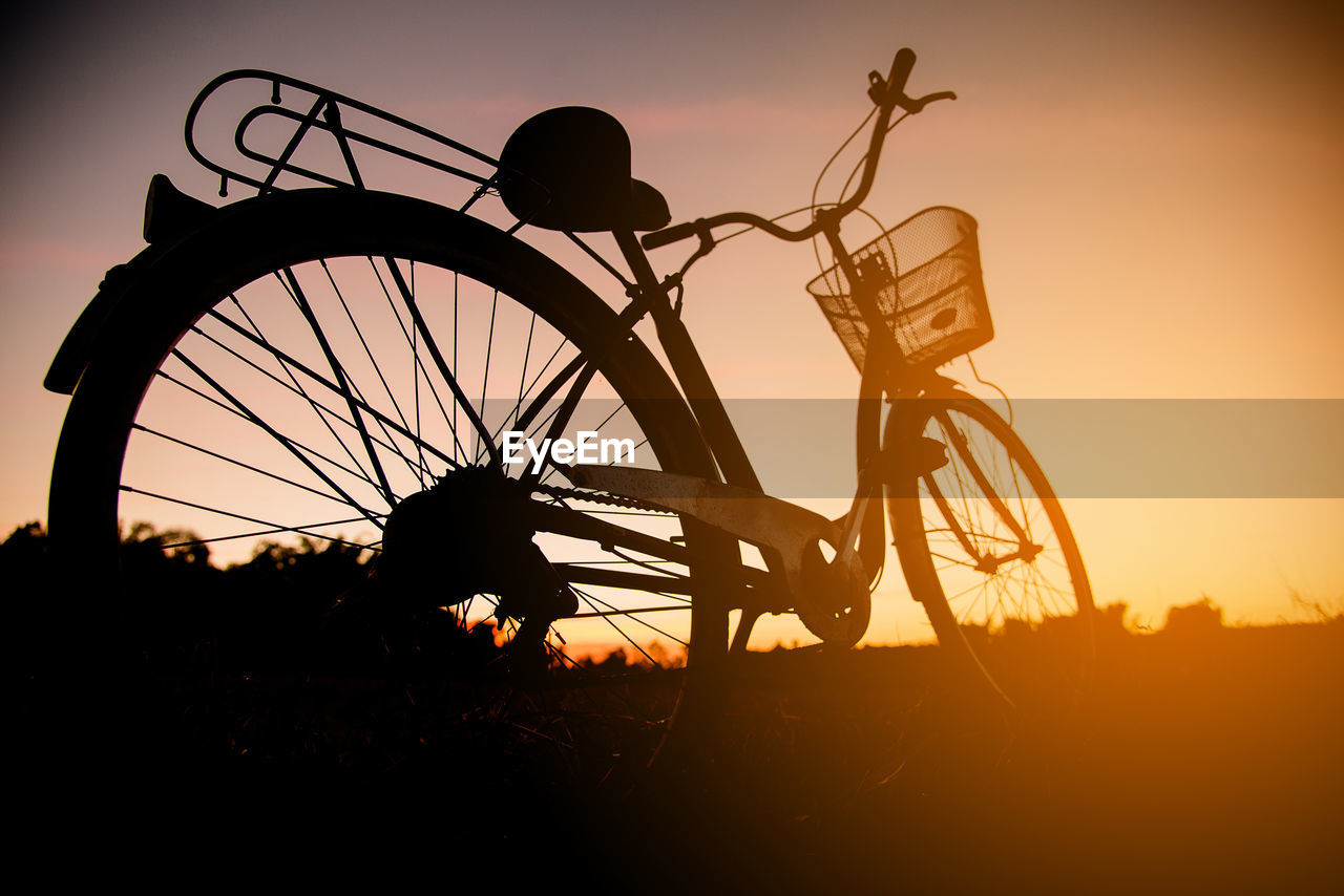 SILHOUETTE BICYCLE ON FIELD AGAINST ORANGE SKY