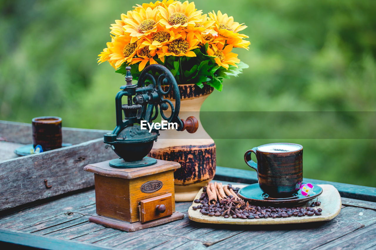 flower, flowering plant, plant, nature, vase, yellow, table, beauty in nature, freshness, wood, no people, food and drink, cup, outdoors, summer, focus on foreground, day, mug, flower head, container, food, multi colored, fragility