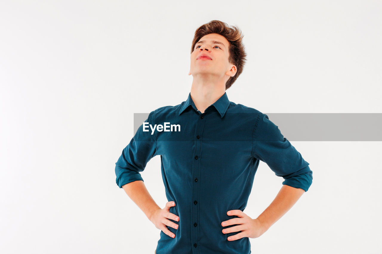 Young man with hands on hip looking away while standing against white background