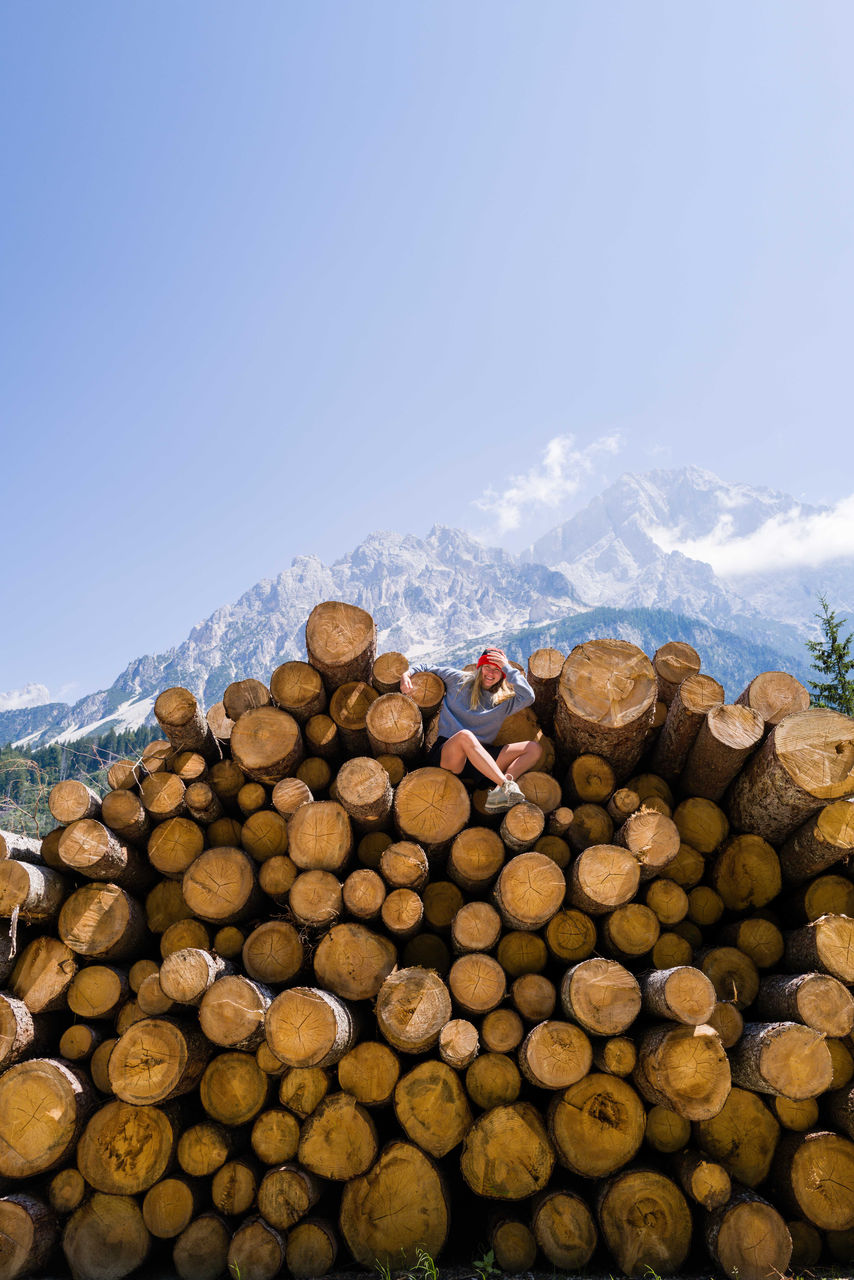 Woman sitting on the stack of the tree logs