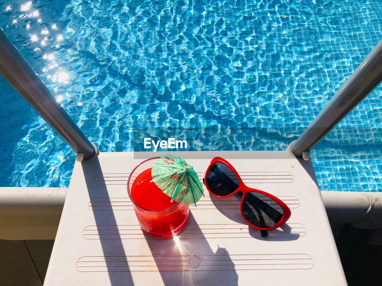 High angle view of drink with sunglasses on steps over swimming pool