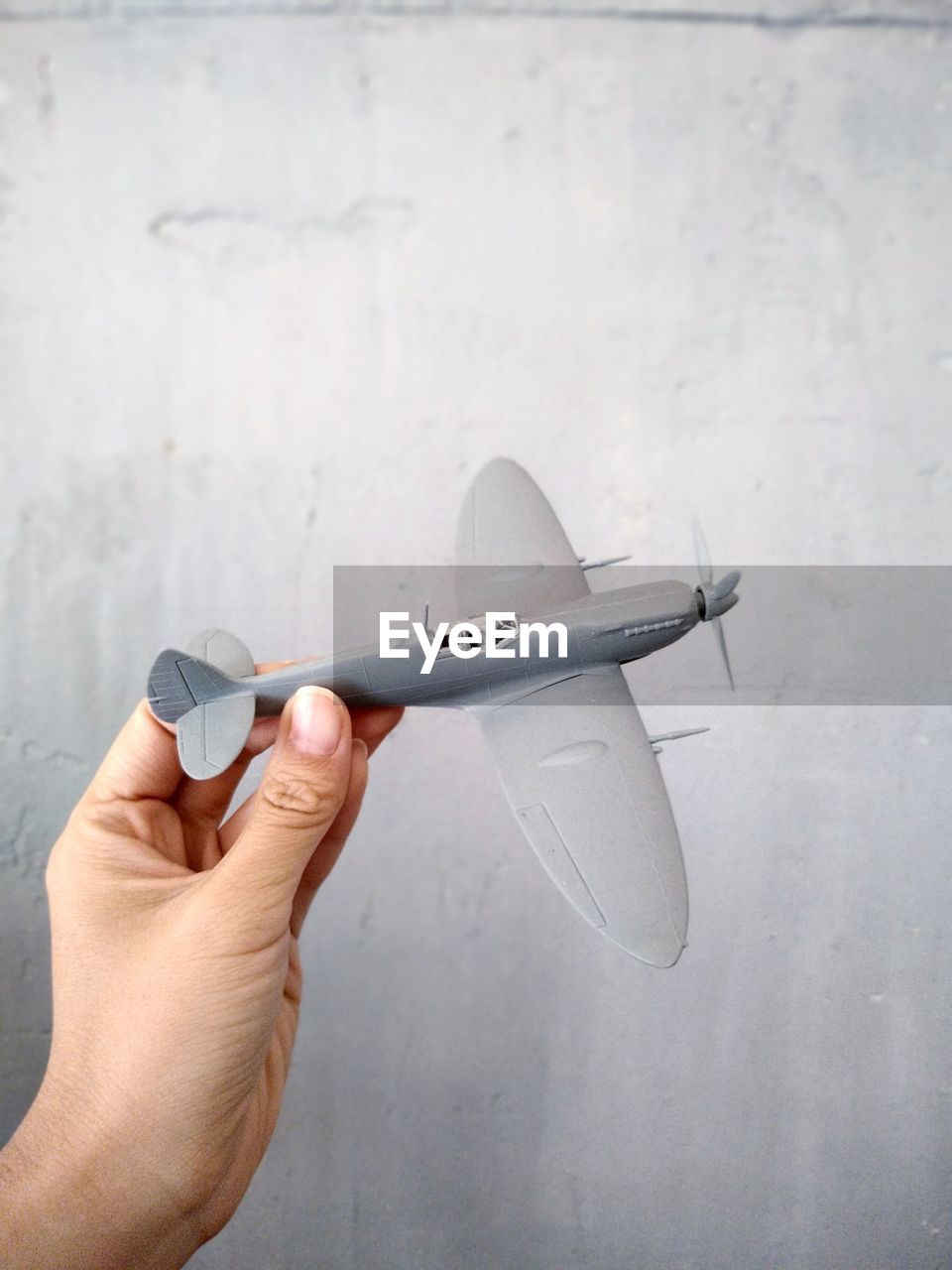 CLOSE-UP OF MAN HOLDING AIRPLANE AGAINST WALL