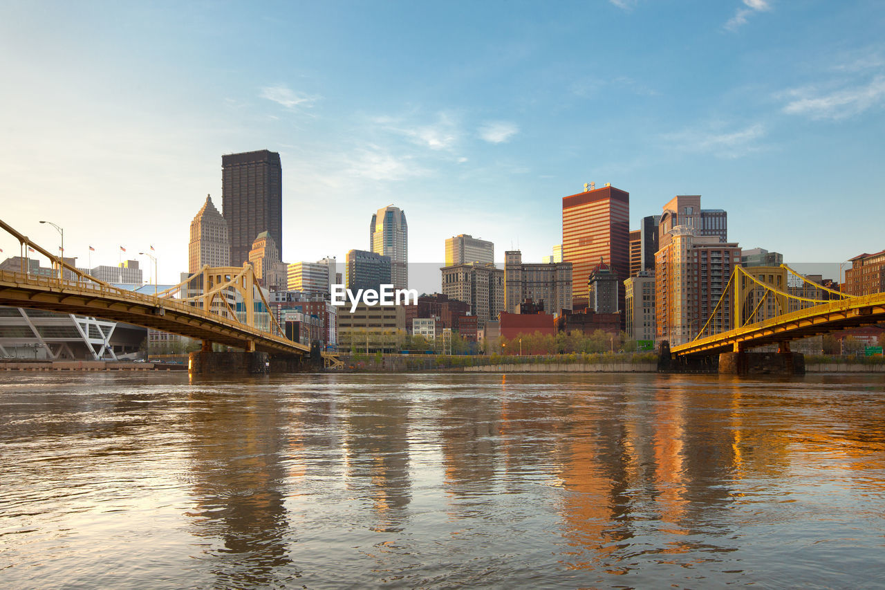 Bridge over river by buildings against sky in city