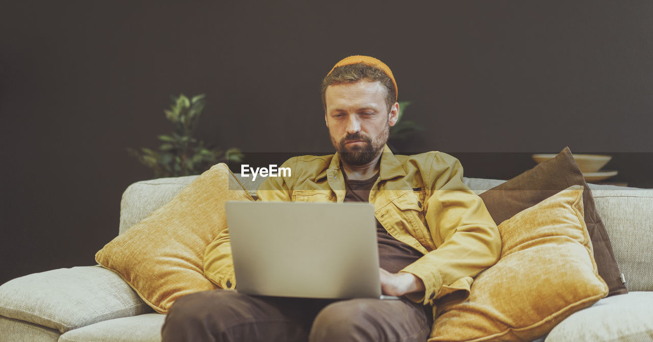 portrait of man using laptop while sitting on sofa at home