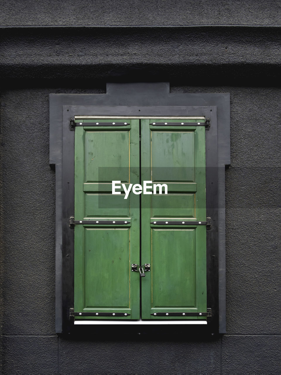 Black wall of building with window locked on wooden green shutters.modern details and vintage style.
