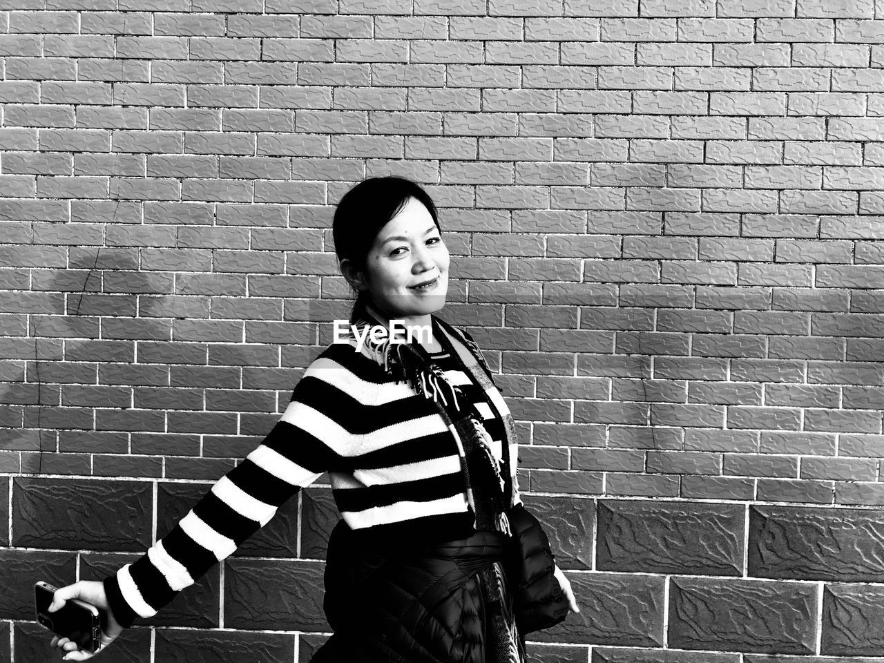 Portrait of smiling woman walking by brick walls