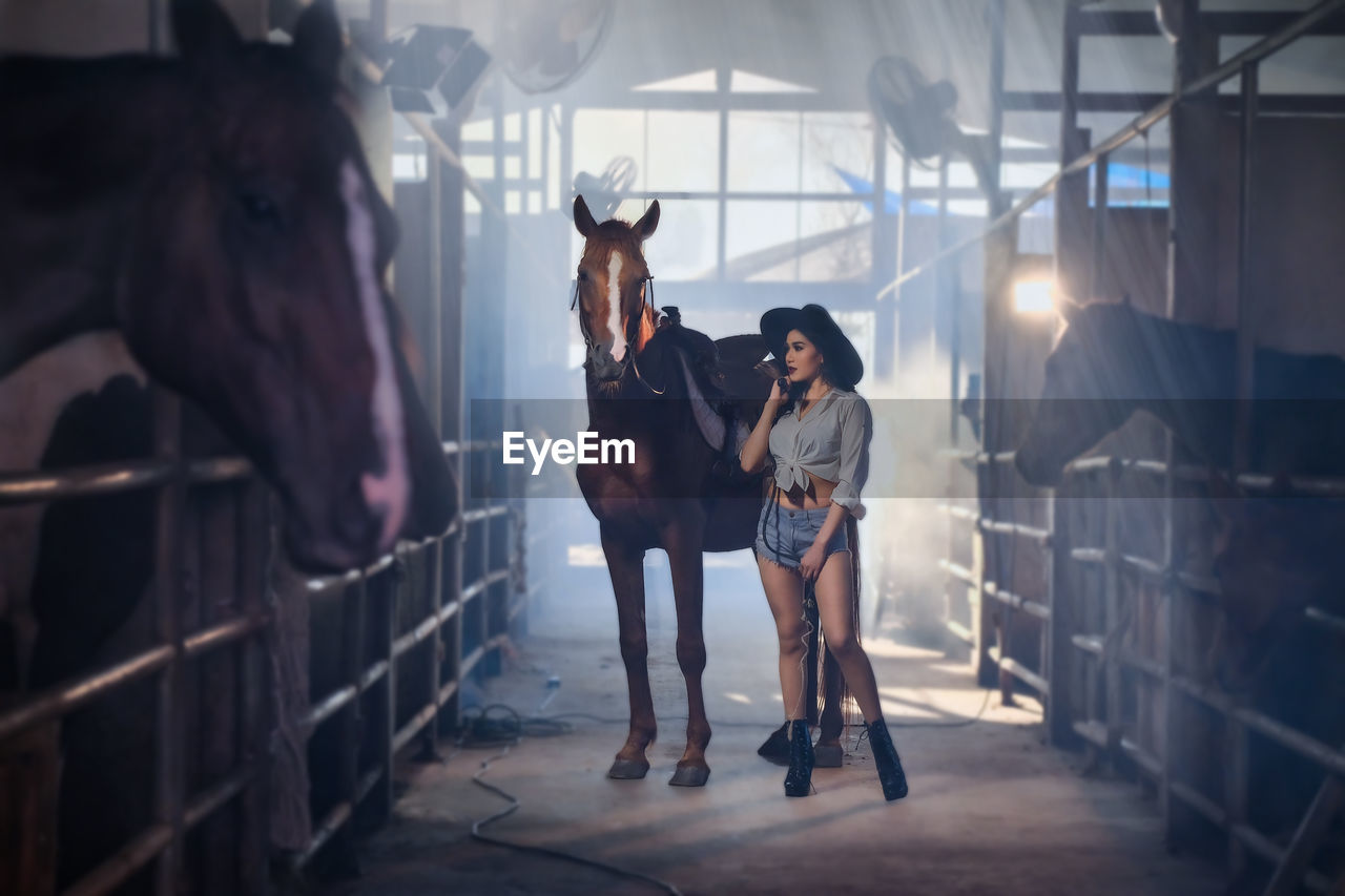 Beautiful woman standing with horse in barn