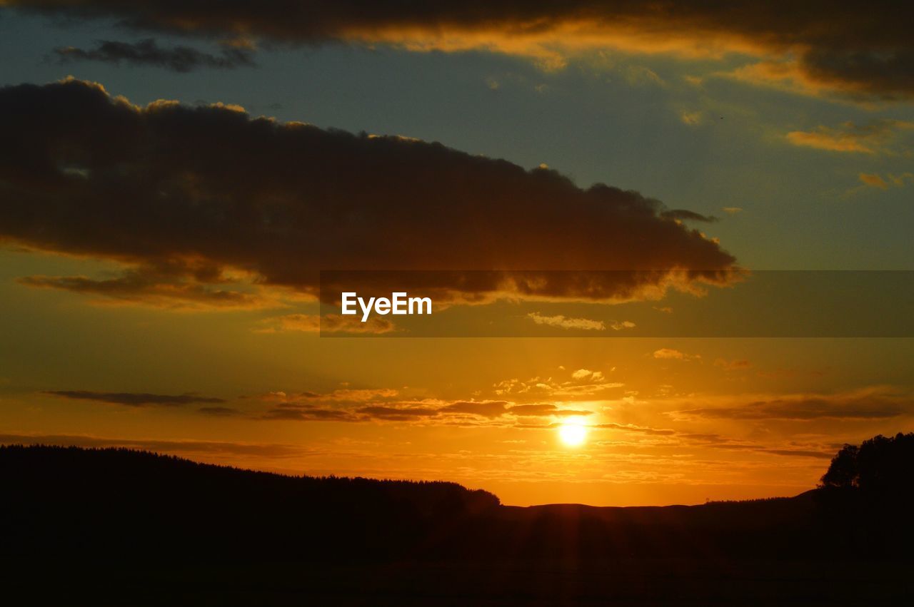 SILHOUETTE OF LANDSCAPE AGAINST CLOUDY SKY DURING SUNSET