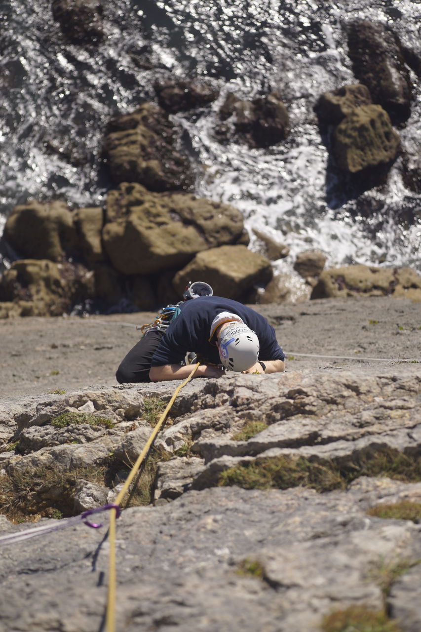 REAR VIEW OF MAN SURFING ON ROCK