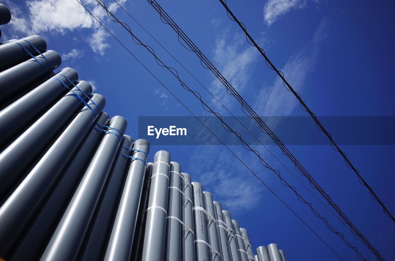 Low angle view of pipes and power lines against blue sky