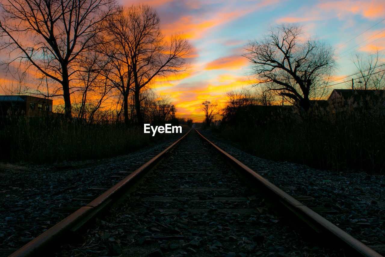 Diminishing perspective of railroad track against sky during sunset