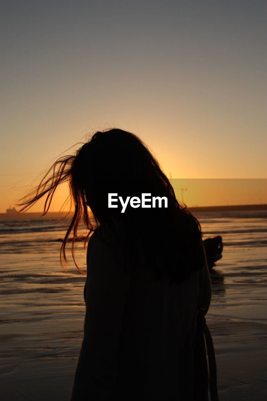 Woman at beach against sky during sunset