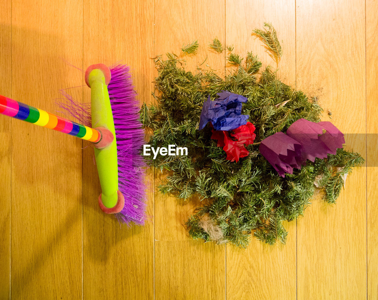 Multi-coloured broom and a pile of pine needles and christmas cracker hats on a wood effect floor