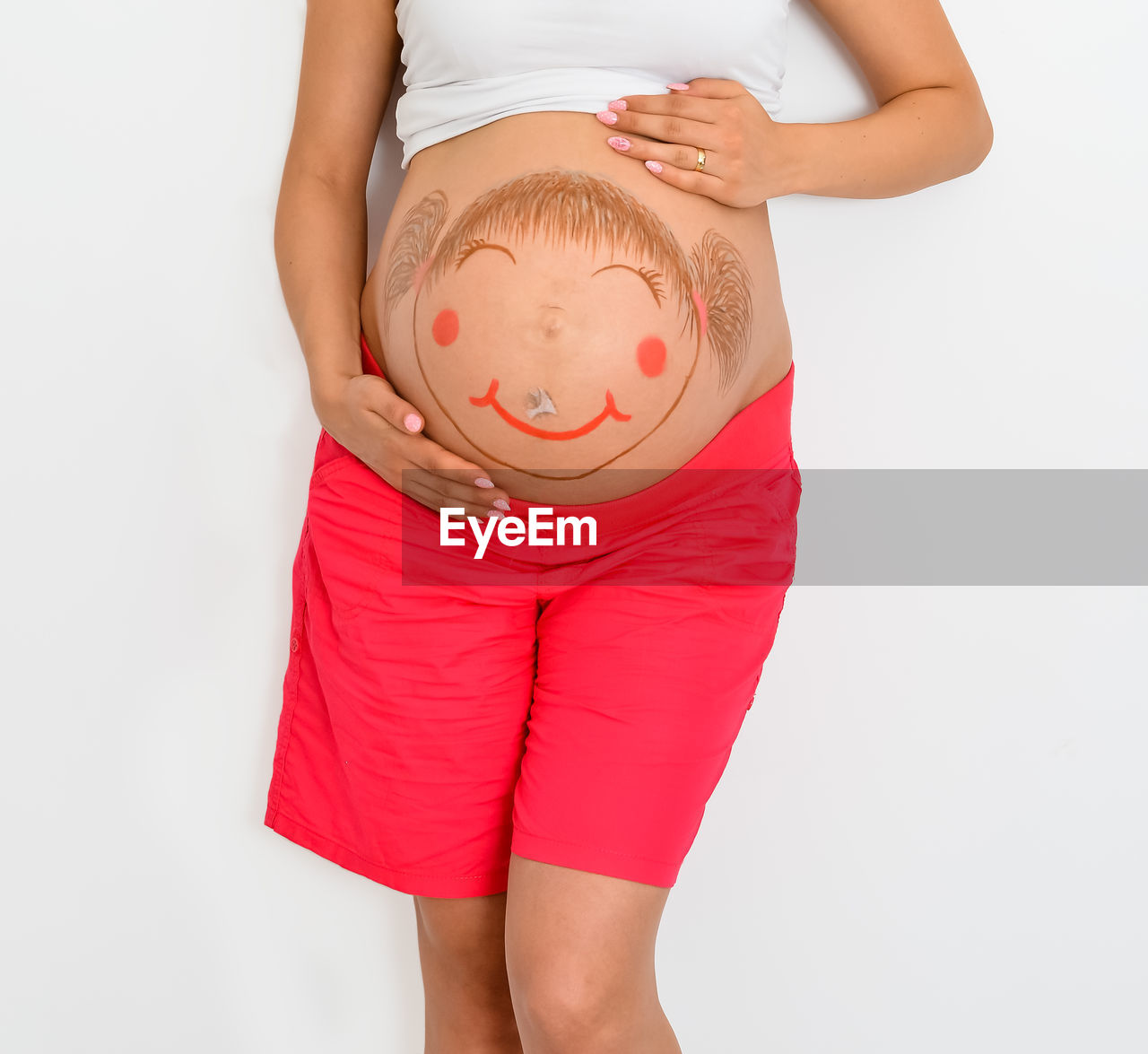 Midsection of pregnant woman with painting belly standing against white background