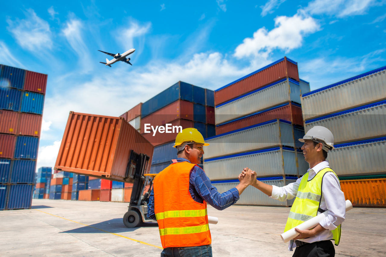 Workers shaking hands while standing against cargo containers at commercial dock