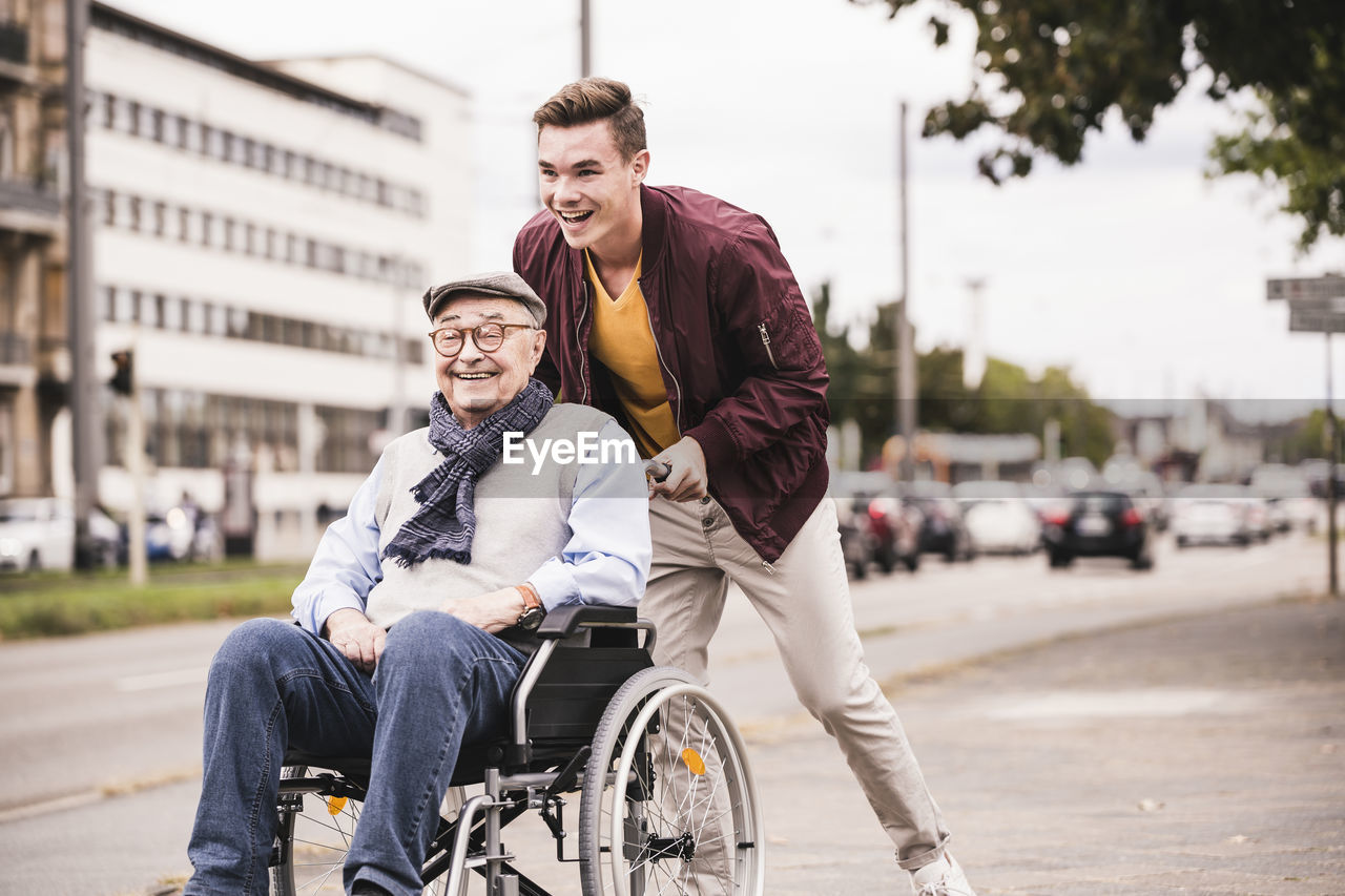 Laughing young man pushing happy senior man in wheelchair
