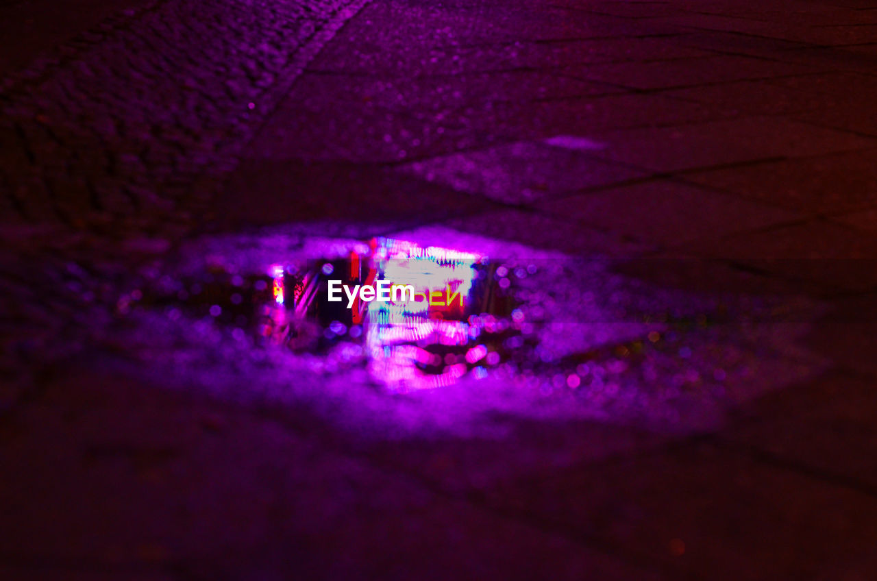 Illuminated open sign reflecting in puddle at night