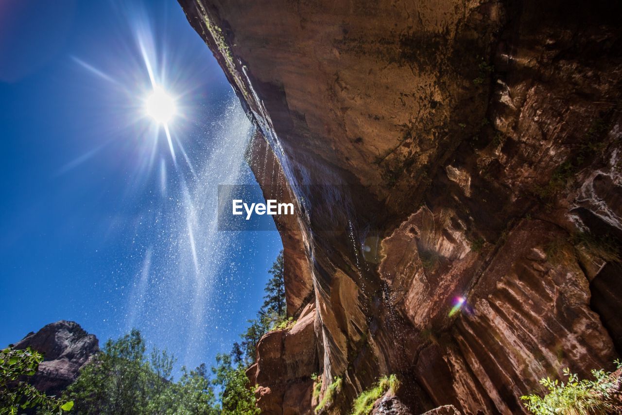 LOW ANGLE VIEW OF SUN SHINING OVER ROCKS