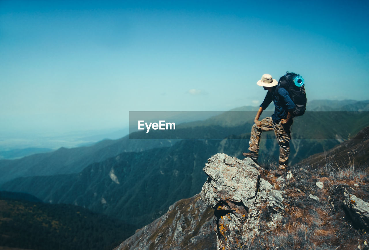 Backpack man standing on cliff against sky