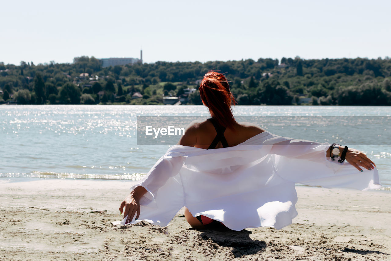 Back view of carefree woman with arms outstretched relaxing at the beach in summer day.