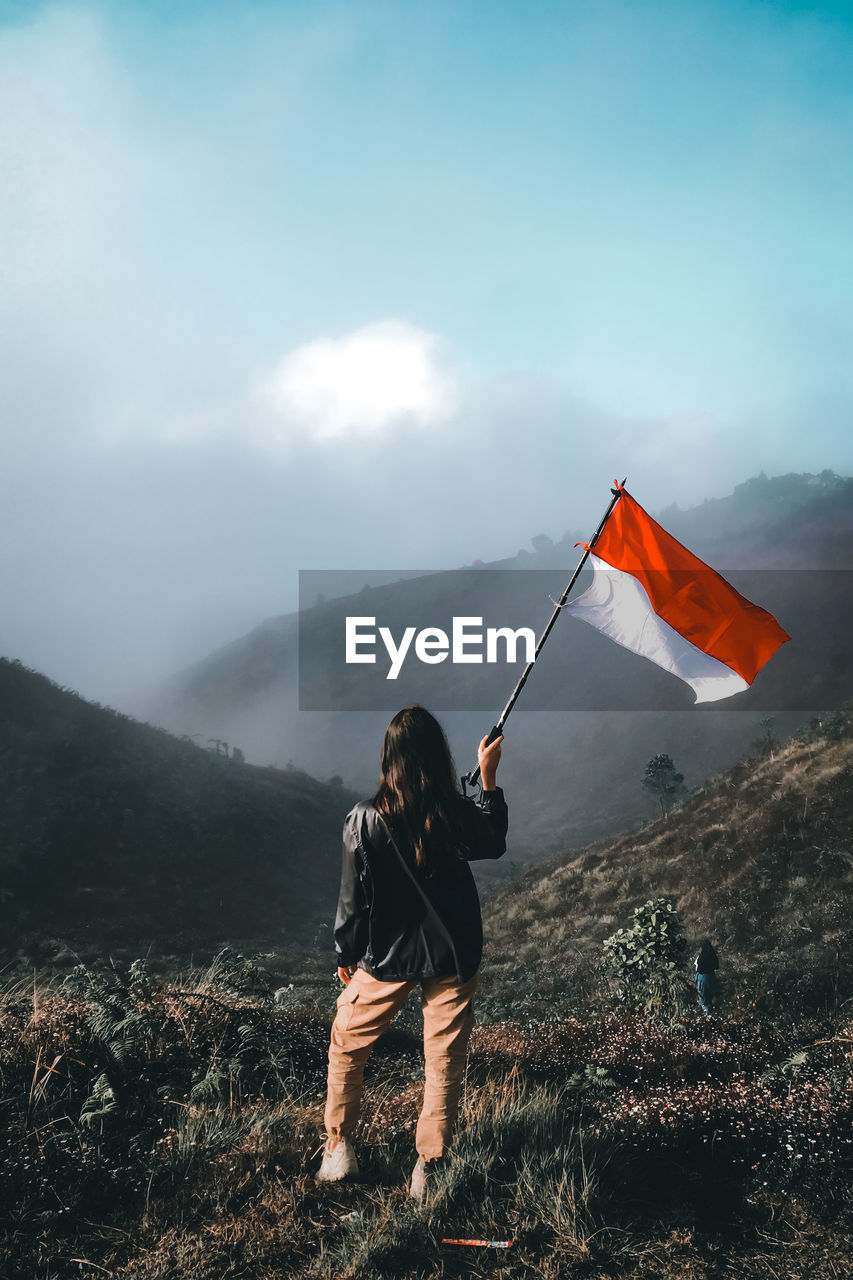 Woman standing with flag on field against mountains