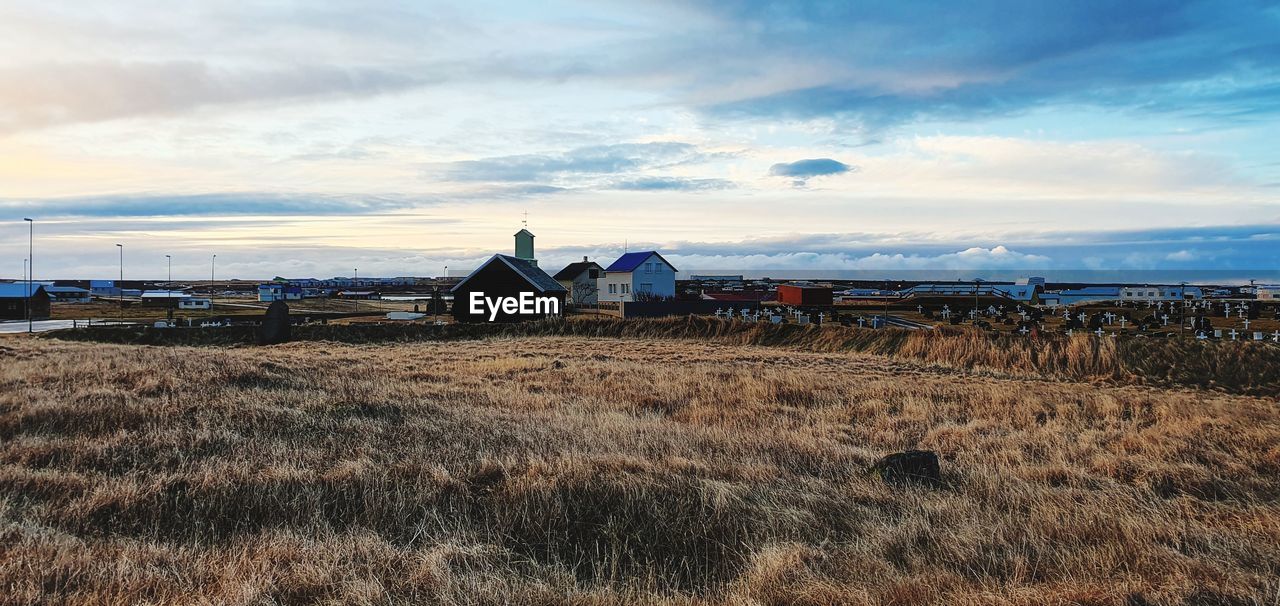 HOUSE ON FIELD BY HOUSES AGAINST SKY