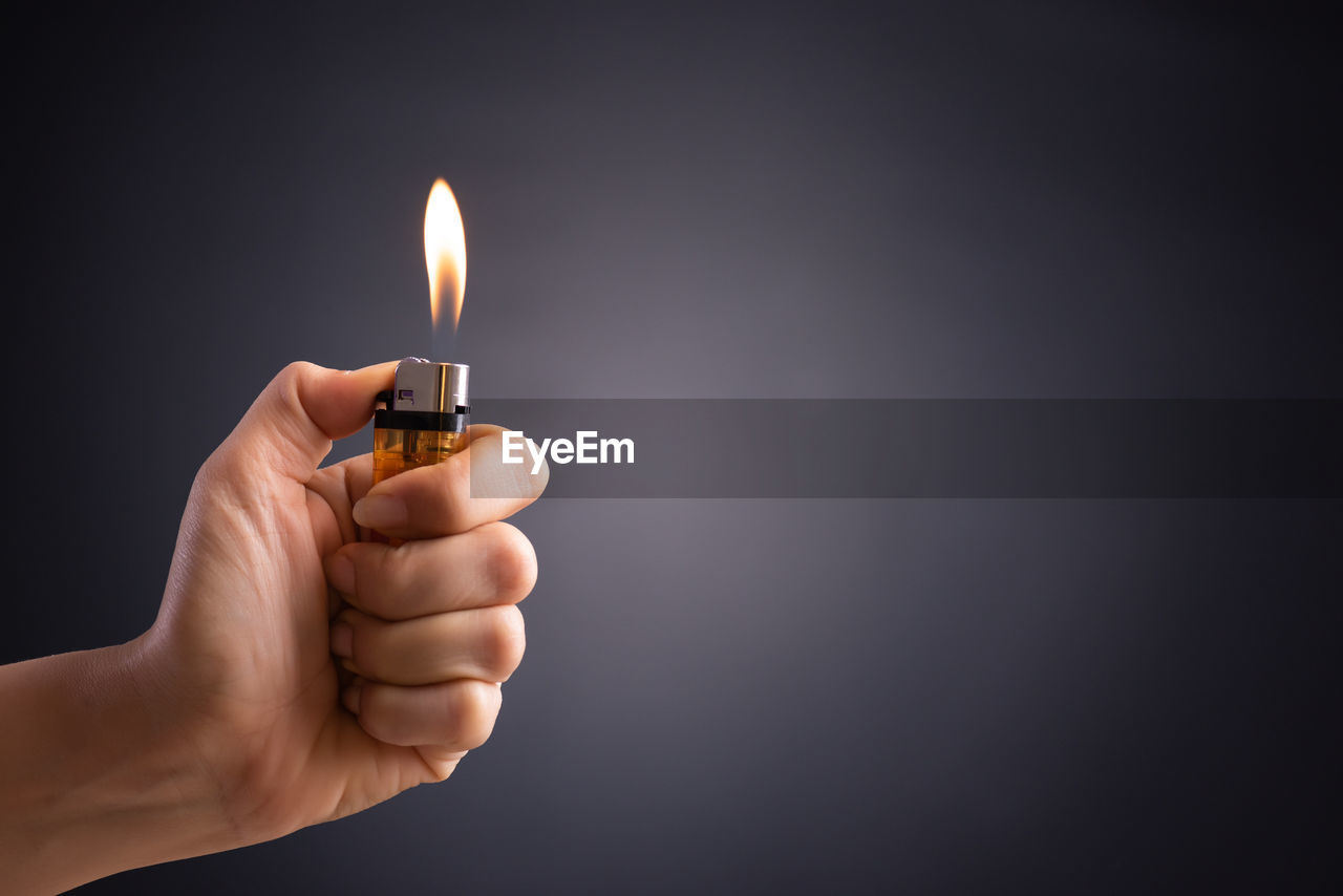 Close-up of hand holding cigarette lighter against gray background