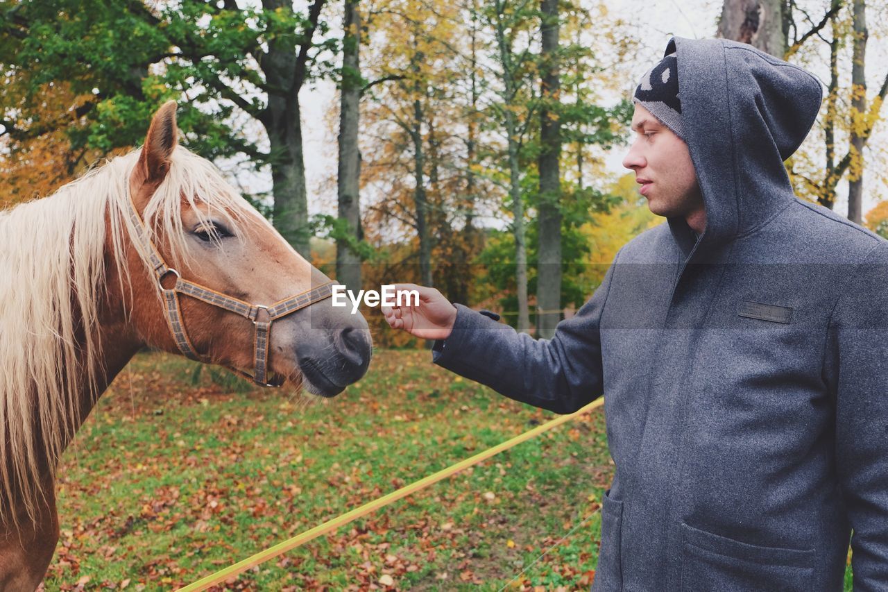 Man in hooded shirt standing by horse on field during autumn