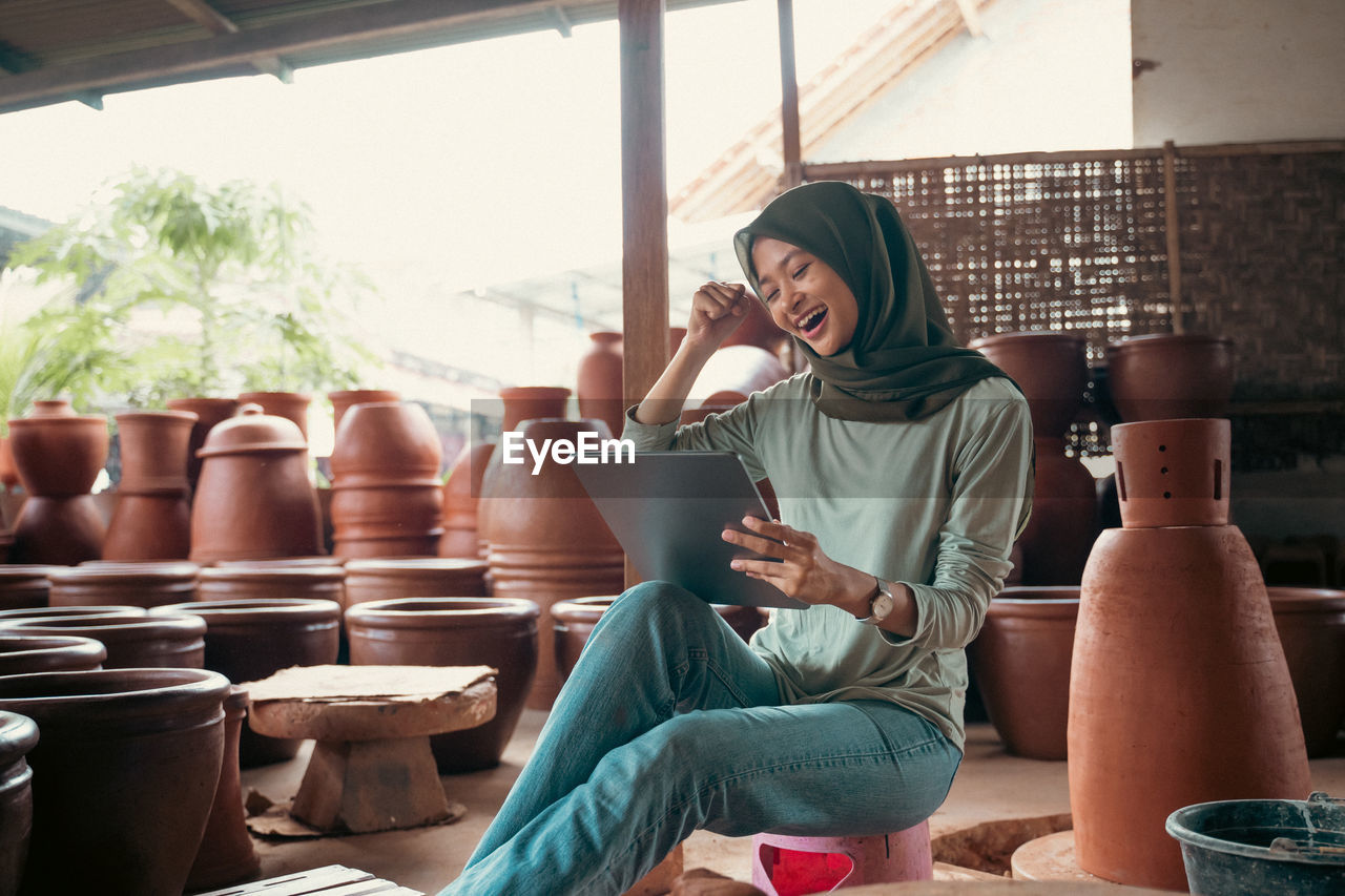 Smiling woman in hijab using digital tablet at work shop