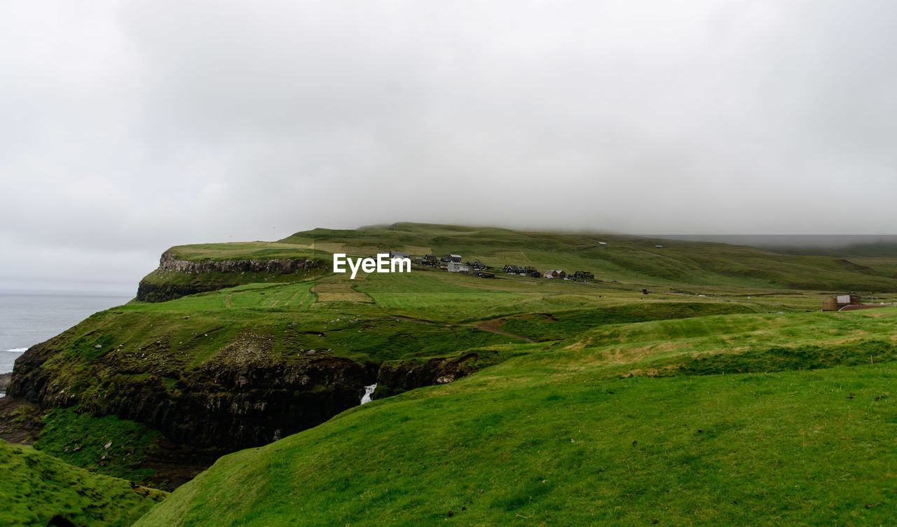 Scenic view of green landscape and sea against sky