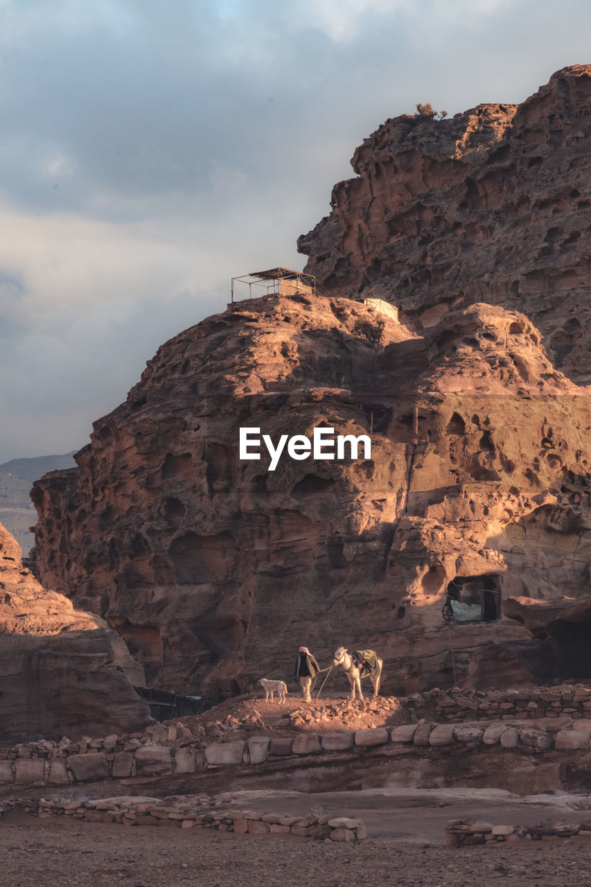 Man with donkey and dog companion in front of rocky terrain.