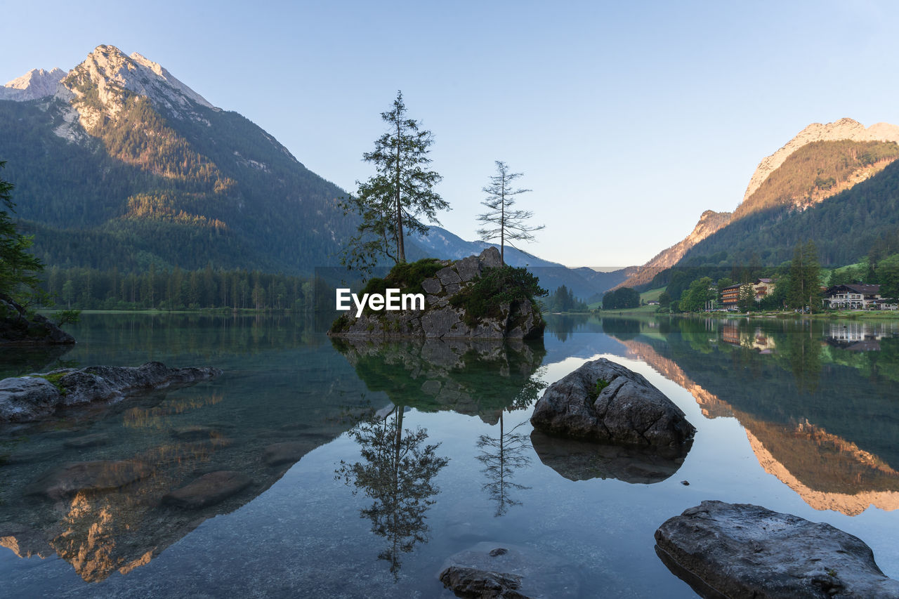 Crystal clear alpine tarn with rocky islands with tree on them during sunrise, hintersee, germany