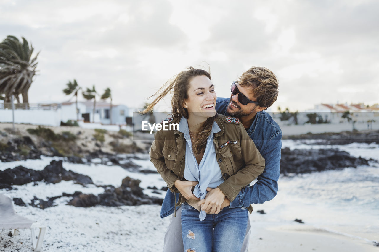 Smiling man embracing woman from behind at beach