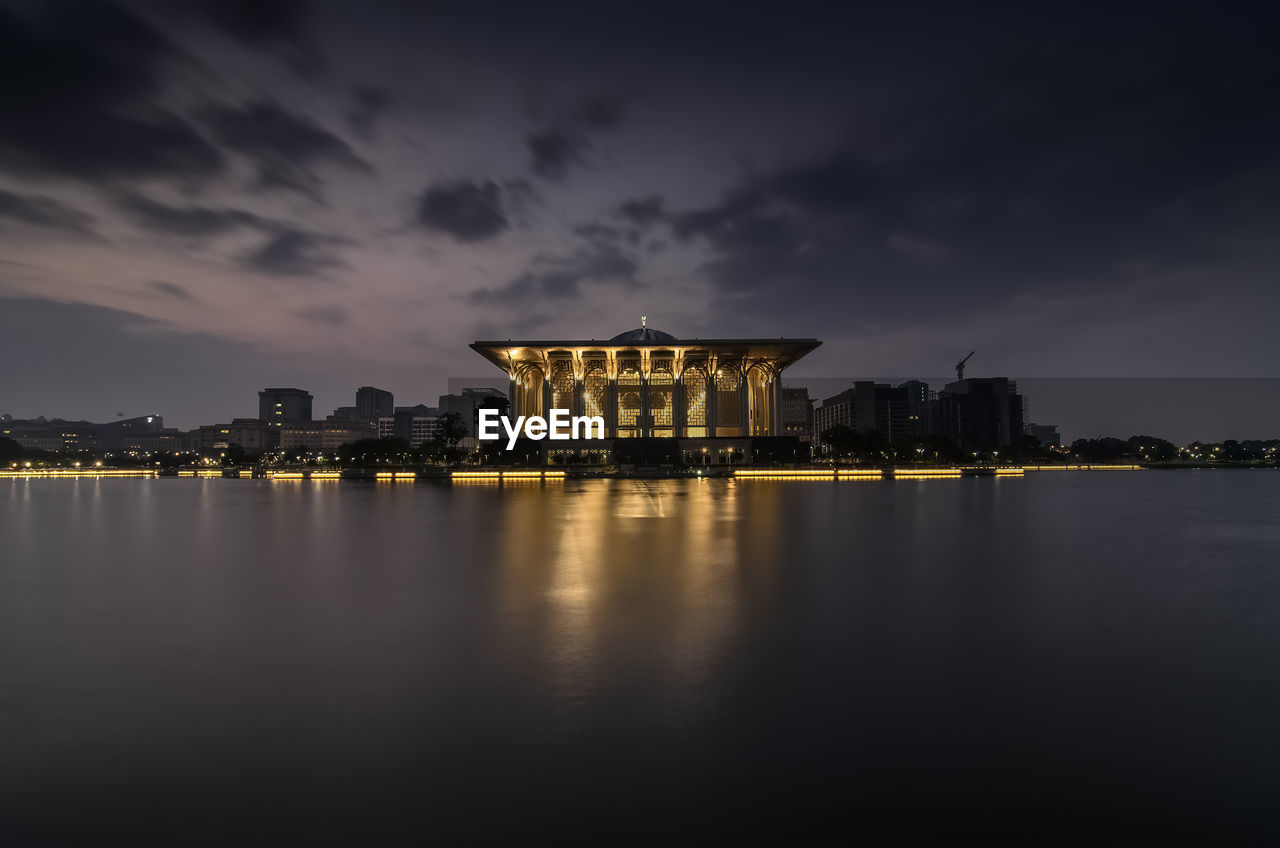 Illuminated iron mosque and lake against cloudy sky during sunrise