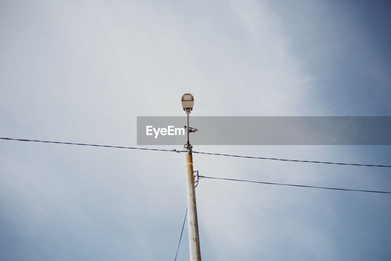 Low angle view of street light with cables against sky