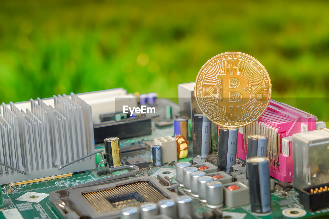 Close-up of bitcoins with motherboard against grassy field