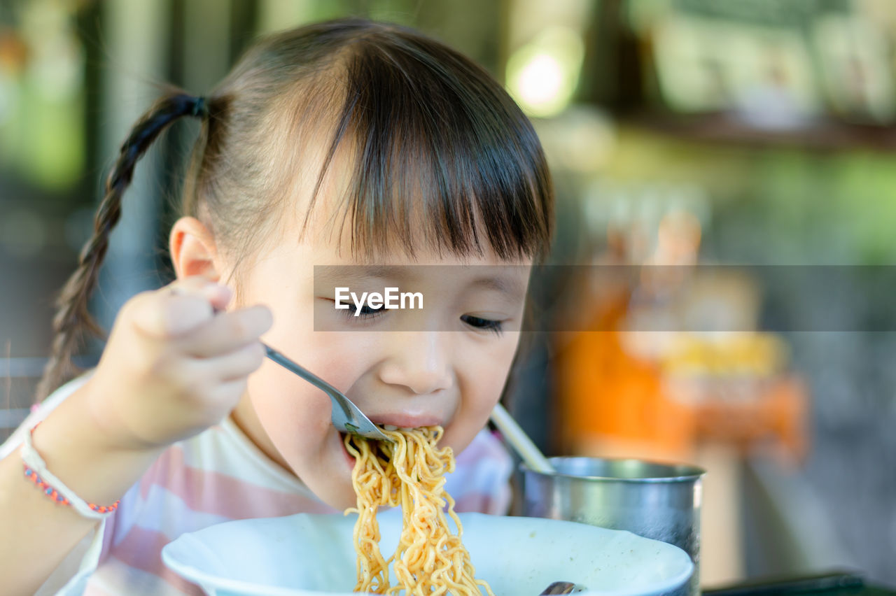 Portrait of cute girl eating noodles at restaurant