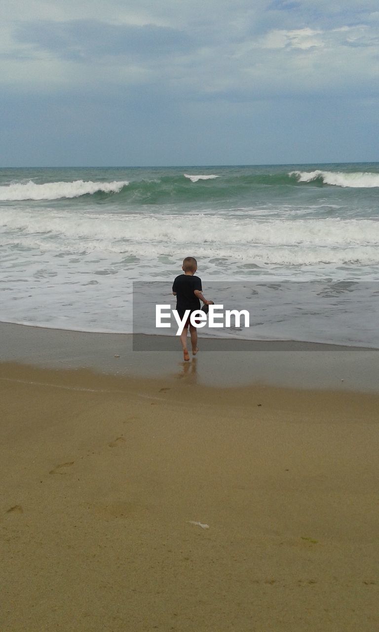 Rear view of boy walking on shore at beach