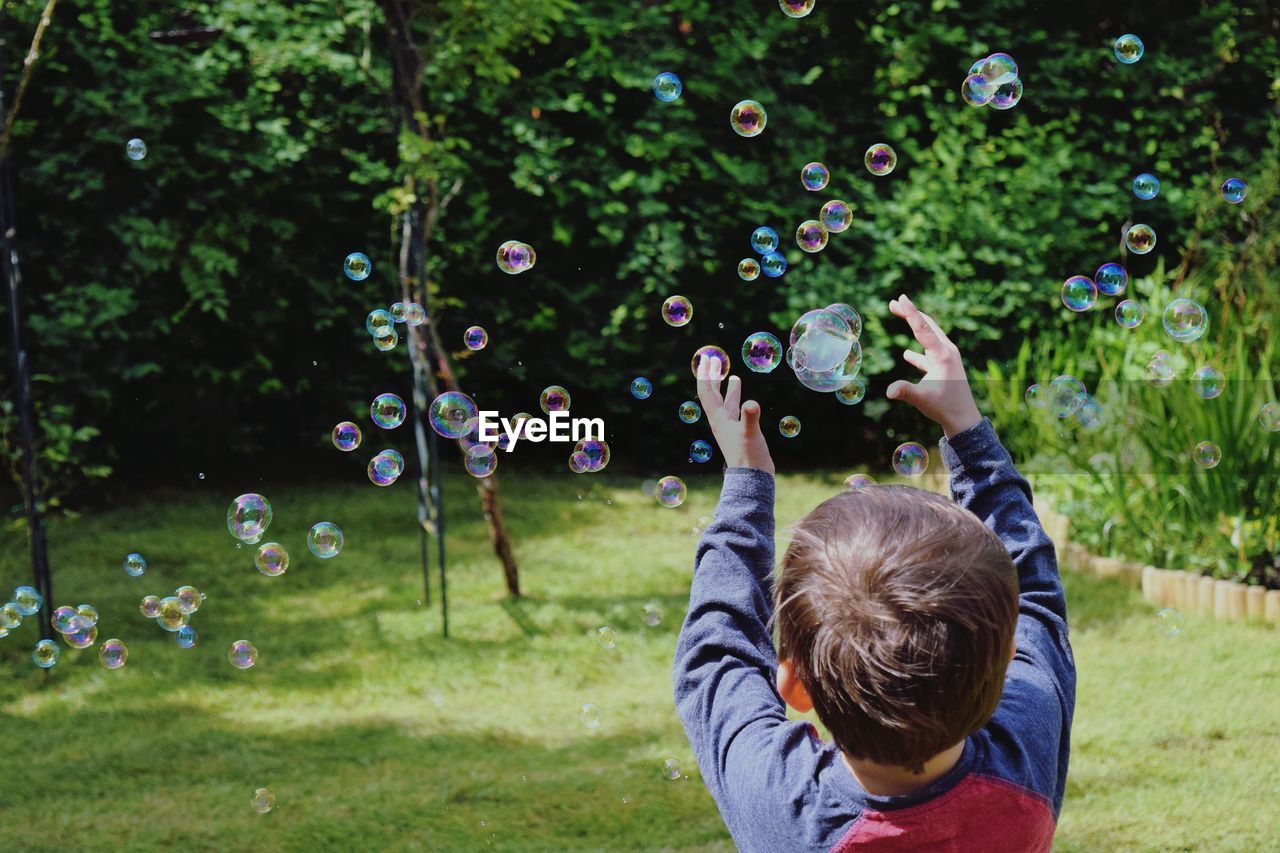 Rear view of boy catching bubbles in park