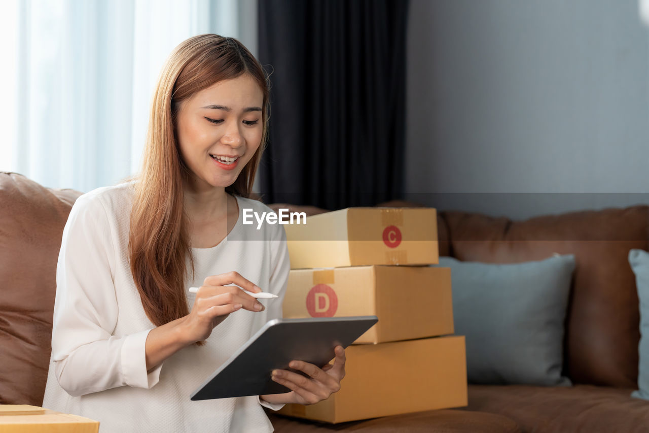 portrait of smiling woman using digital tablet while sitting on sofa at home