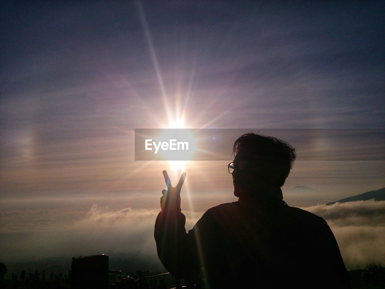 Silhouette man holding sun against sky during sunset