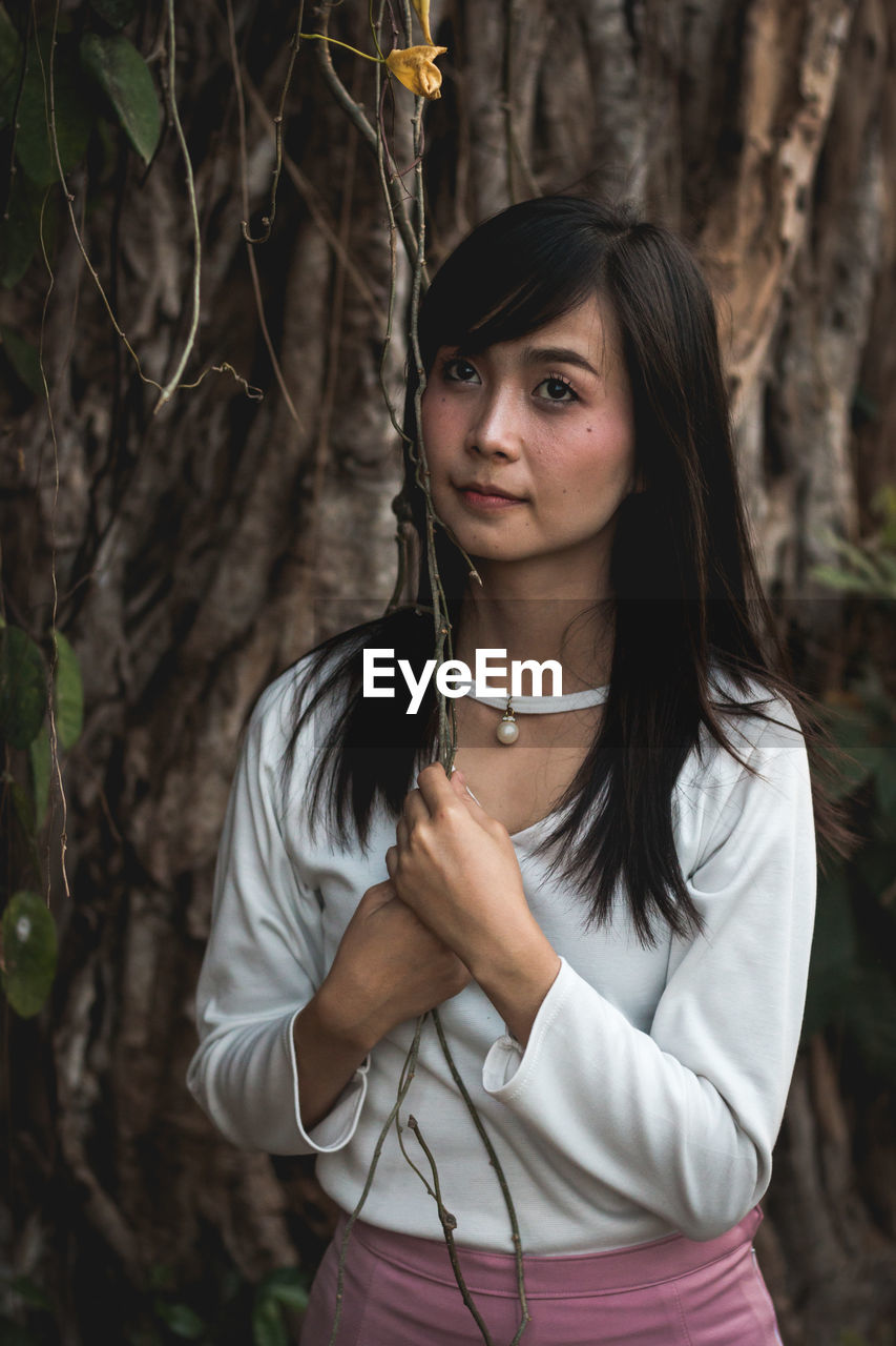 Thoughtful young woman standing against tree in forest