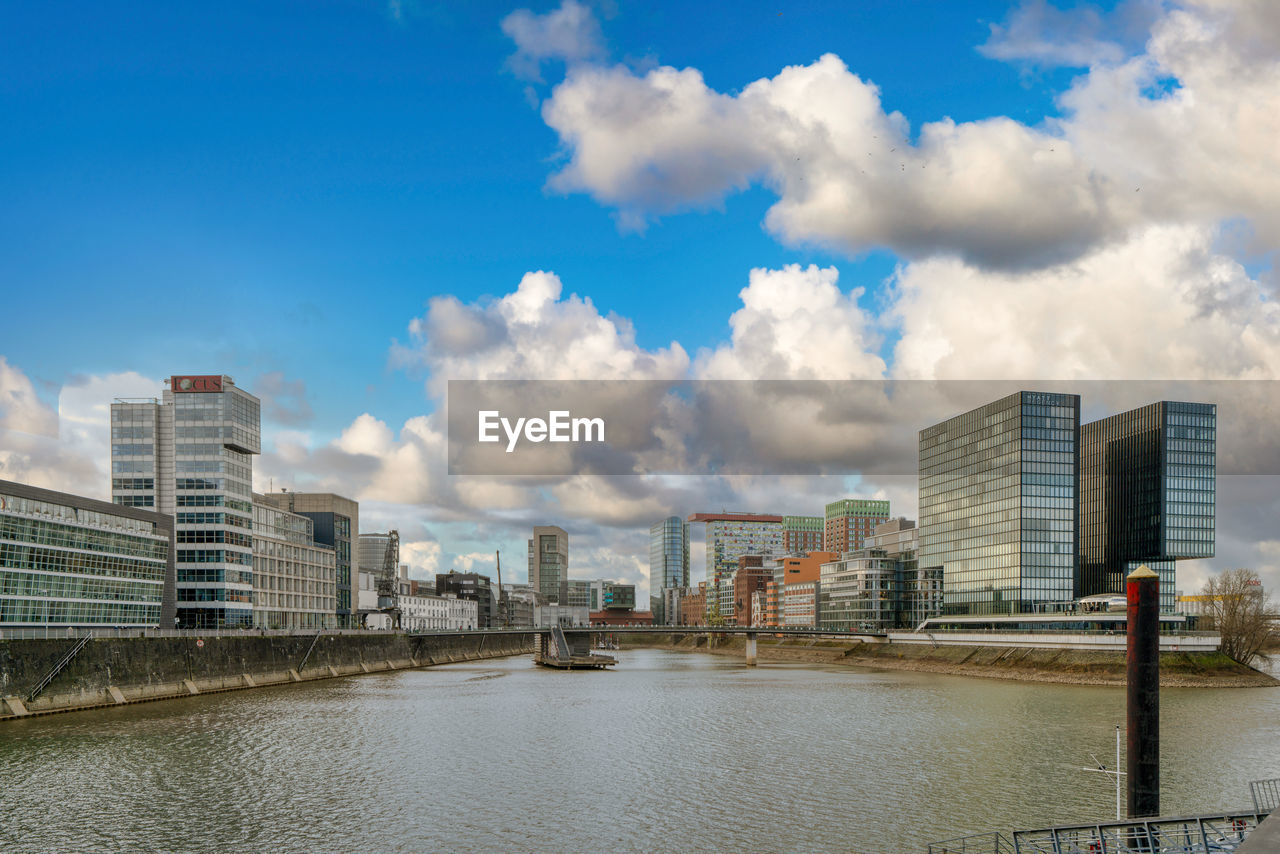 Buildings by river against cloudy sky