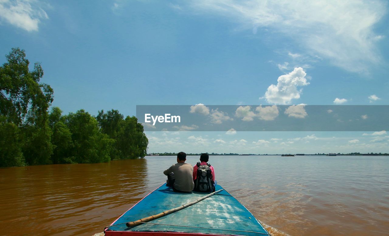 Rear view of friends sailing on boat in river against sky