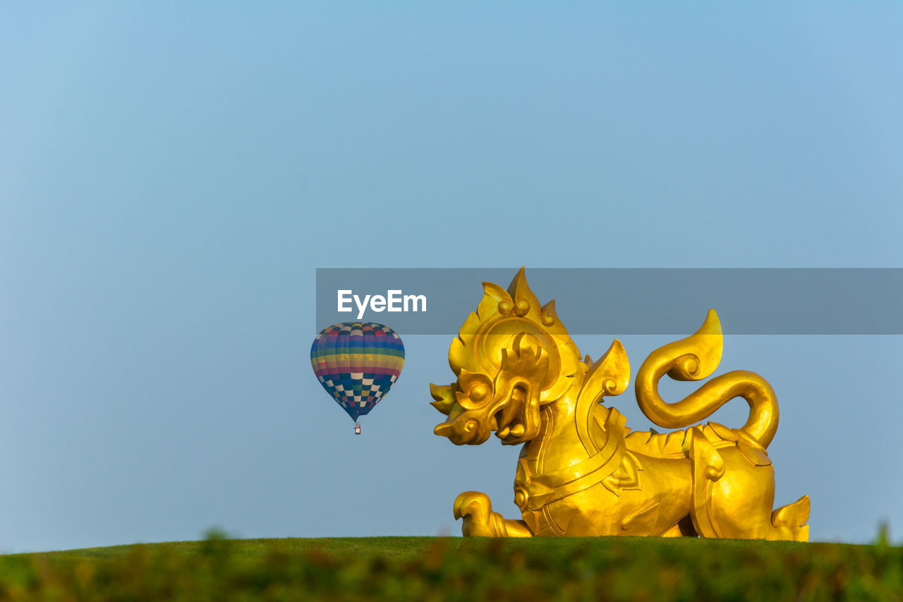 Golden statue with parachute against clear blue sky