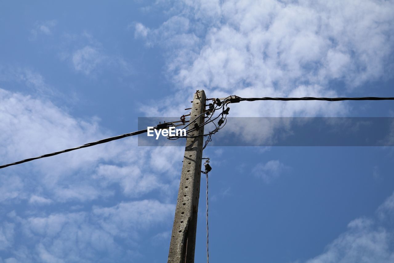 Low angle view of electricity cables on concrete pole against blue sky