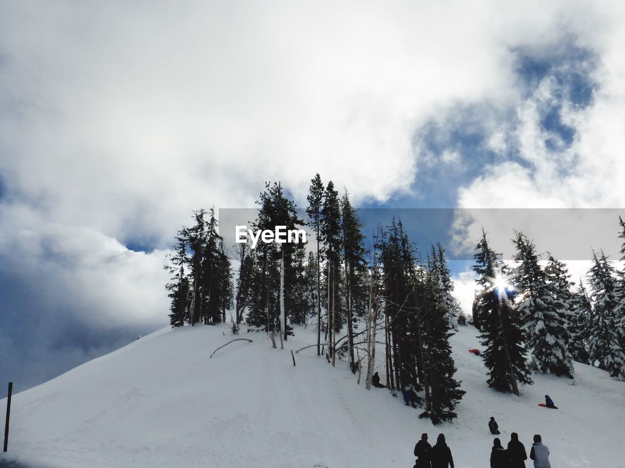 Rear view of people standing on snowcapped mountain against cloudy sky