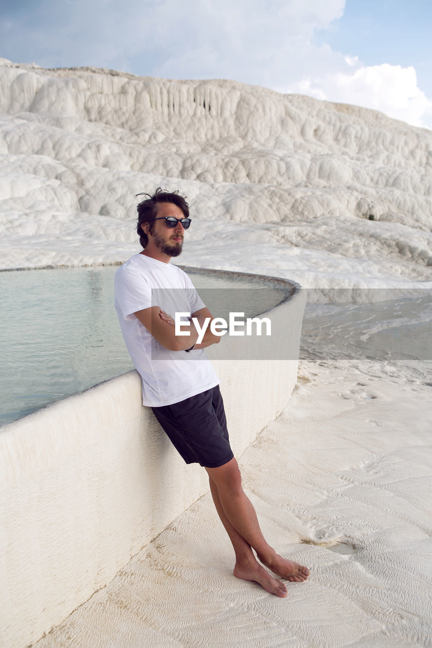 Man with a beard in a white t-shirt and shorts rest on a white mountain in pamukkale