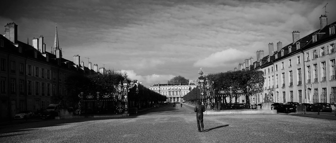 Man walking on footpath amidst buildings in city against sky